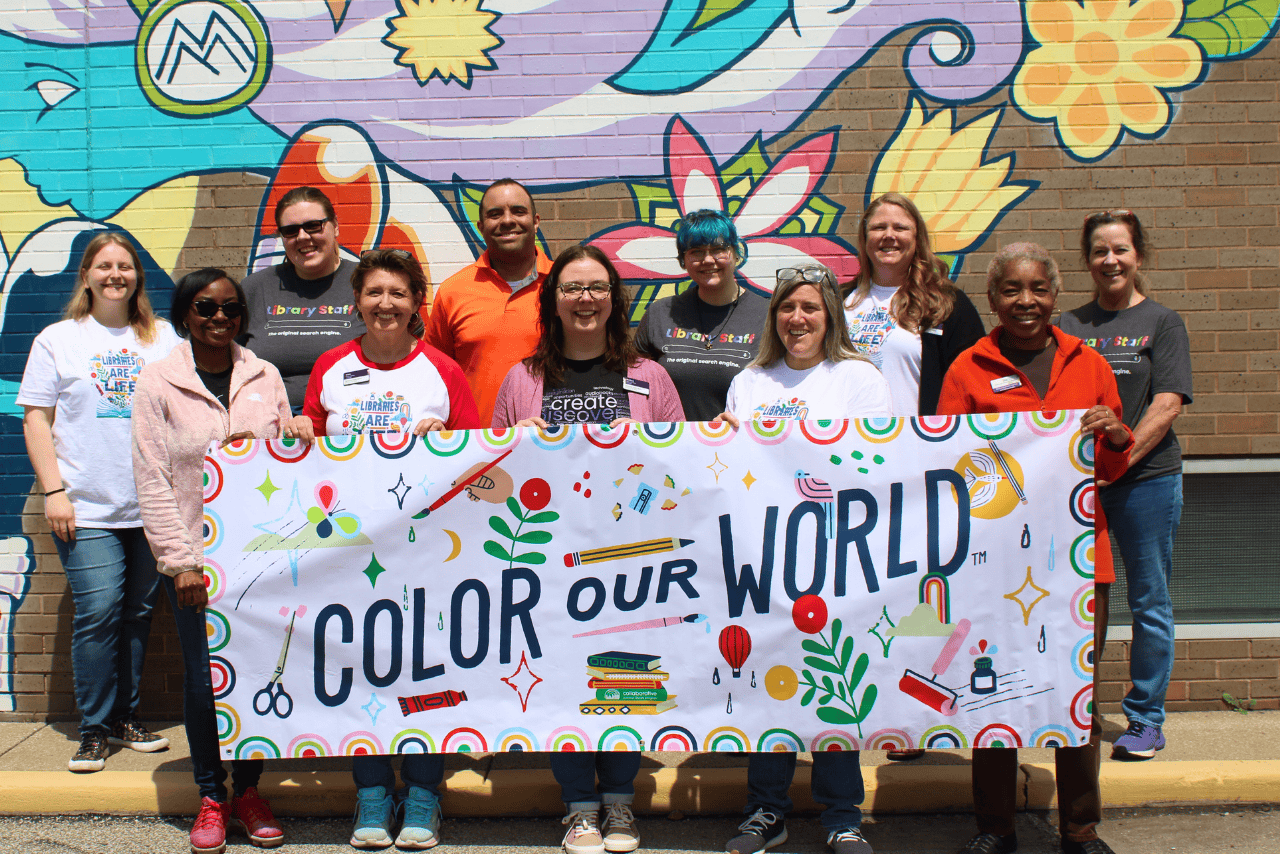 A group of library staff standing with a banner that reads 'Color Our World.'