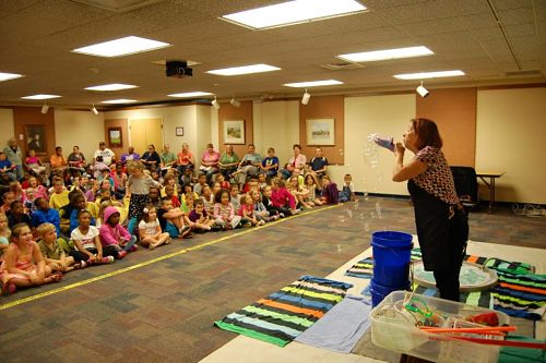 the bubble lady performer blows bubbles out of a croc shoe to a crowd of children in the Spillette Meeting Room